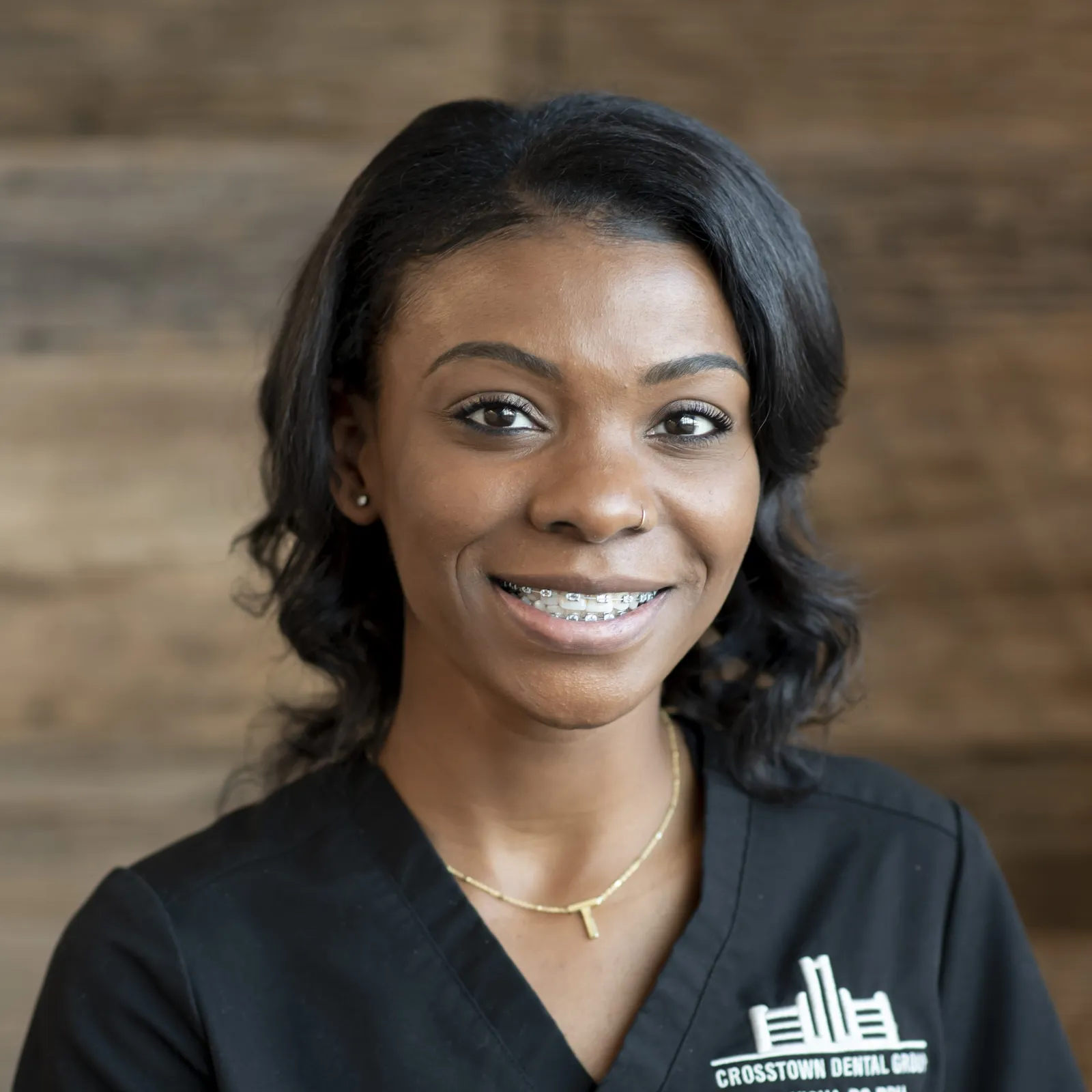 Smiling woman with braces wearing a black Crosstown Dental Group shirt and necklace.