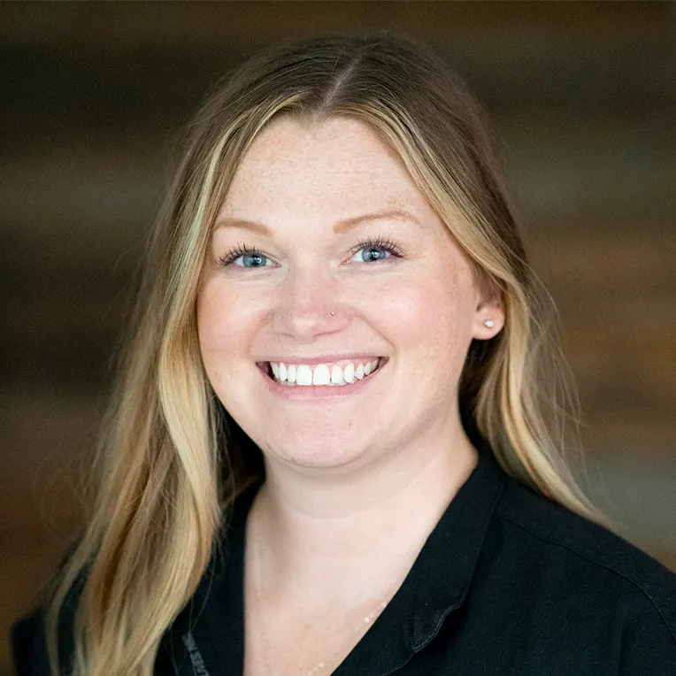 Smiling woman with long blonde hair wearing a black collared shirt indoors.